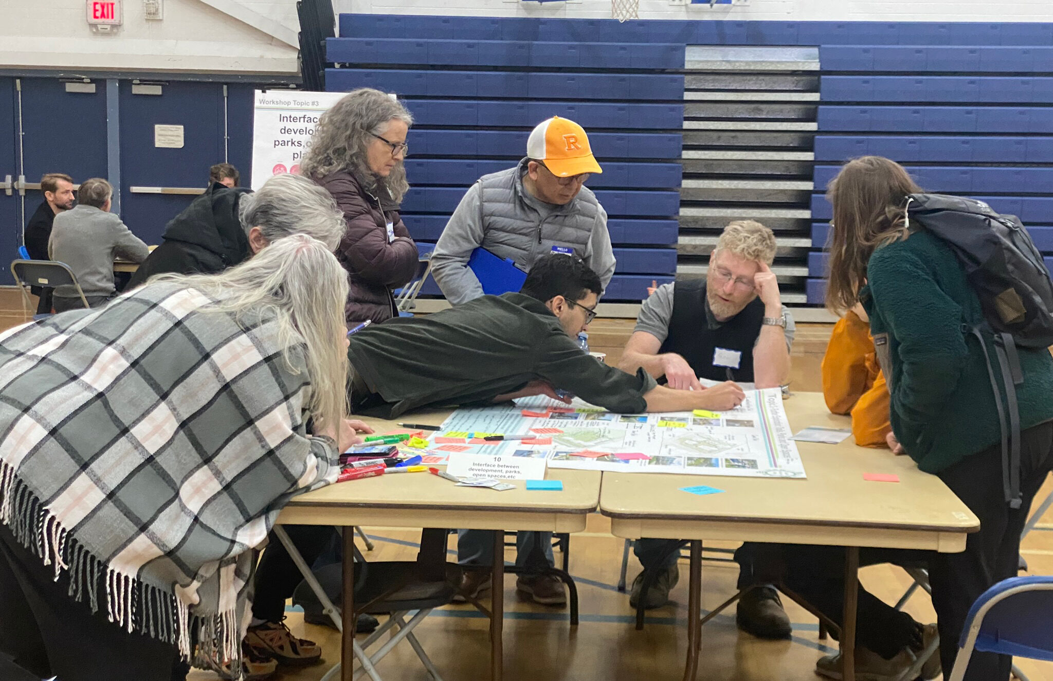 People gather around the table, pointing towards the map.