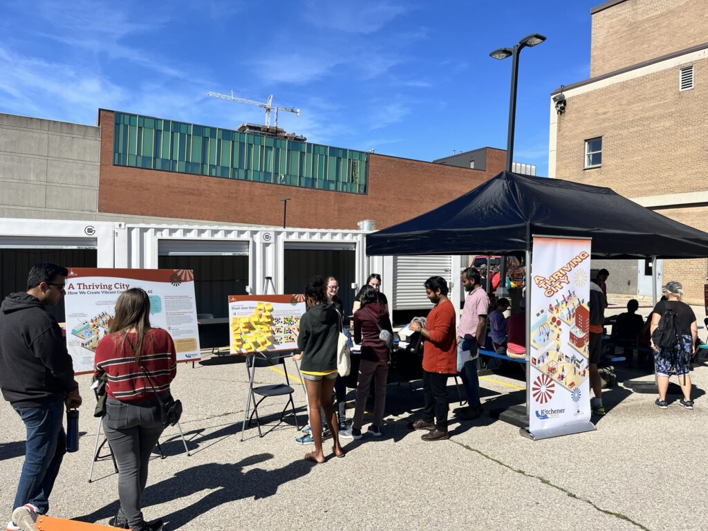 Several people gathering around panels at the Thriving City station for the Block Party engagement event.