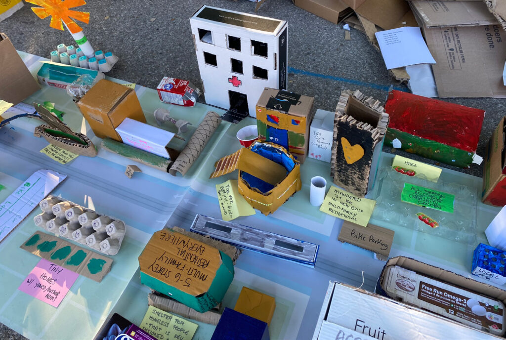 Upcycled materials from the Upcycled City activity at the Block Party engagement event. The table contains items like painted egg carton treys, boxes, and paper towel rolls.